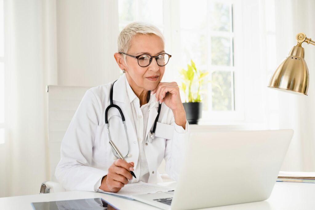 Doctor in white coat working on laptop, looking for diagnosis, telemedicine with patient at hospital